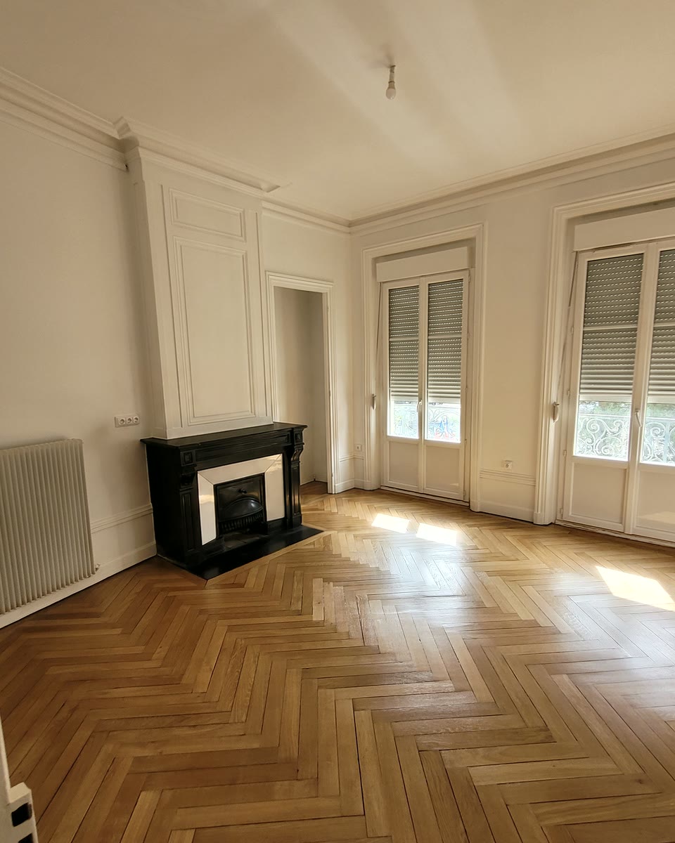 Salon rénové : murs et moulures blancs, parquet et cheminée noire à Saint-Étienne